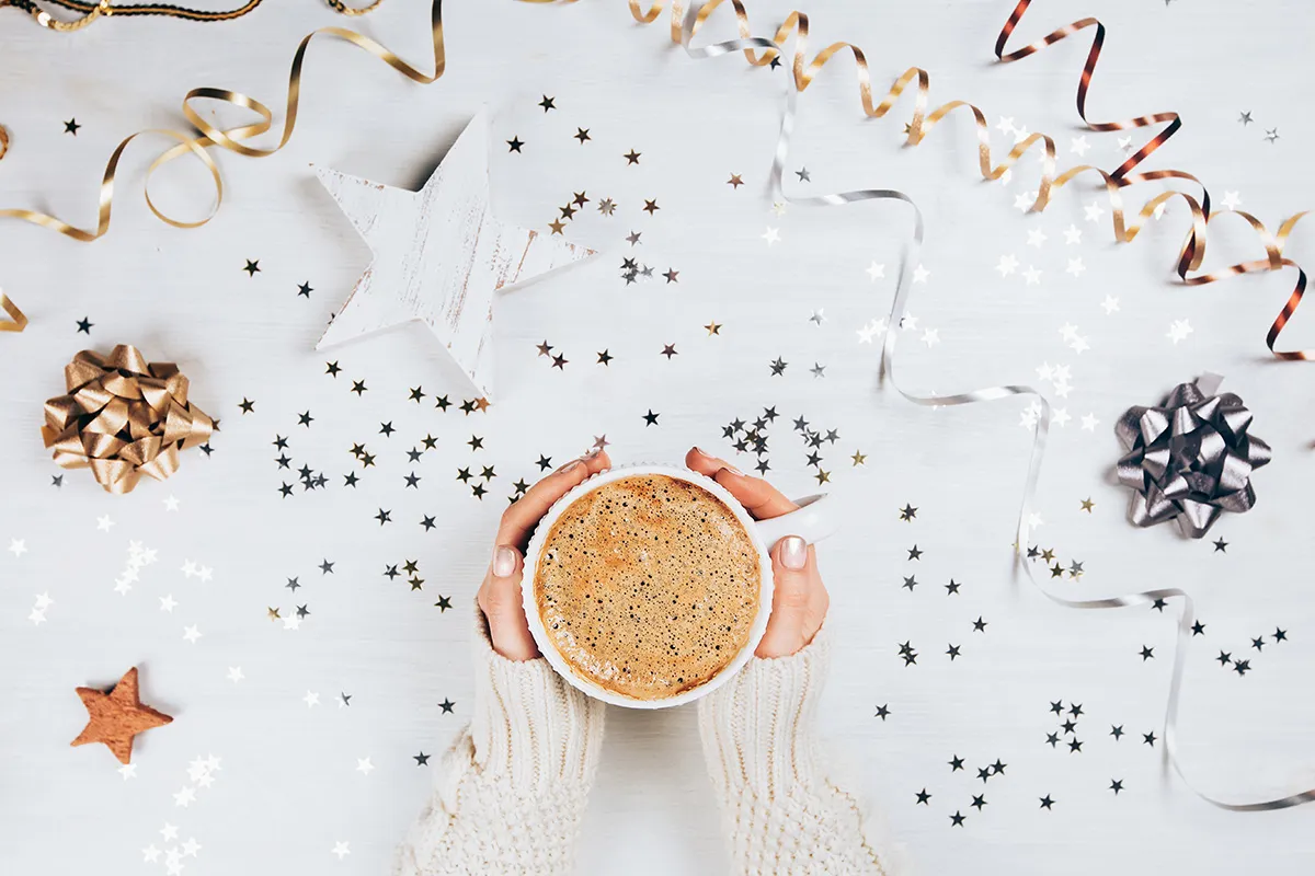 holiday decorations surrounding hands holding a warm beverage